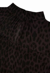 Blusa de estampado de leopardo con una tela transparente y texturizada. Patrón en púrpura oscuro y negro con un escote alto y detalles fruncidos en la parte trasera.