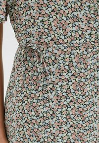 Vestido de envoltura floral en negro con pequeñas flores rosas, azules y verdes. Presenta un cinturón anudado en la cintura y mangas cortas. Tejido ligero.