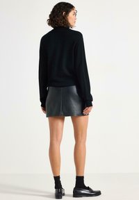 Sort sweater med en afslappet pasform, lange ærmer og ribbede manchetter, sat sammen med en sort læder mini-skirt. Skinnende tekstur, minimal detaljering.