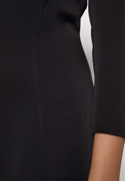 Musta kleit sujuvast kangast, mis on nöörimisega disainitud, pikkade varrukatega ja peente õmbluste detailidega. Klassikaline, mitmekülgne ese.