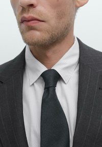 Grau gestreifter Anzugjacke, weiß gestreiftes Hemd und schwarze strukturierte Krawatte. Nahaufnahme des Kragens und des Krawattenbereichs. Sauberes, maßgeschneidertes Aussehen.
