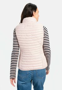 Lichtroze puffer vest met verticale quilt en een hoge kraag. Gelaat over een zwart-wit gestreepte longsleeve shirt. Casual pasvorm.
