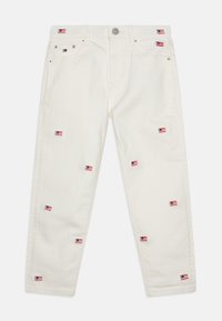 Vaqueros de mezclilla blanca con múltiples parches de bandera bordados en rojo, blanco y azul. Diseño de pierna recta con cinco bolsillos y herrajes metálicos.