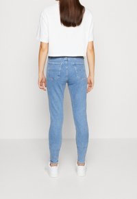 Jeans ajustados azules de denim, con una cintura alta, dos bolsillos traseros y un ligero estiramiento. Combinados con una camiseta blanca corta y zapatillas blancas.