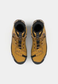 Aukštos viršaus geltoni žygiavimo batai su tekstūruotais juodos gumos padais, rudi batraiščiai ir juodos akcentinės detalės. Lengvos sintetinės medžiagos.