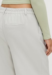 Light gray trousers with an elastic waistband, a single back pocket, and smooth texture, featuring a subtle sheen and relaxed fit.