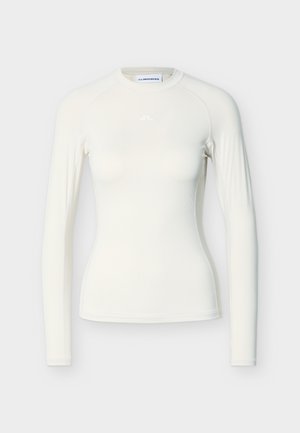 Hosszú ujjú, testhez simuló felső törtfehér színben, sima, rugalmas anyagból készült. Rágslán ujjakkal és a nyakvonal közelében diszkrét logóval rendelkezik.