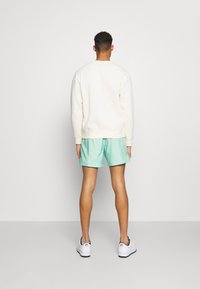 Sweatshirt en polaire crème avec un col rond, associé à un short vert menthe. Des baskets blanches avec des accents noirs complètent le look.