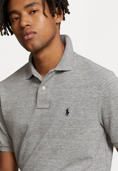 Szara koszulka polo o miękkiej teksturze, z trzema guzikami na plastrze oraz małym czarnym logo na lewej piersi. Krótkie rękawy i dzianinowy kołnierzyk.