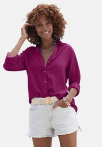 Fuchsia button-up shirt met lange mouwen, gedragen in lichte denim shorts. Het shirt heeft een klassieke kraag en een zachte textuur.