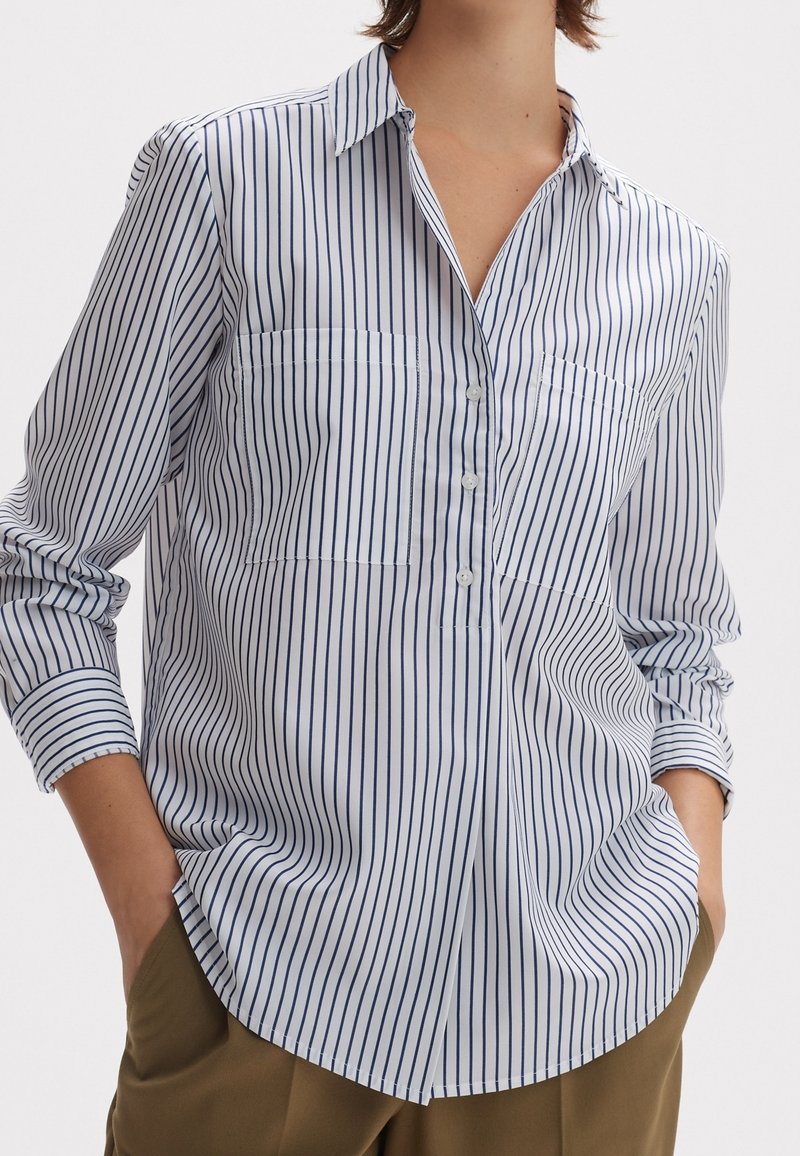 Weißes Button-up-Hemd mit schmalen marineblauen vertikalen Streifen, ausgestattet mit langen Ärmeln, einem Kragen und zwei Brusttaschen. Glatte Textur.