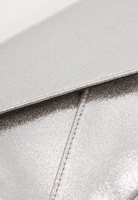 Pochette argentée texturée avec une finition lisse et brillante, dotée d'un rabat pliant et de détails de couture subtils le long des bords.