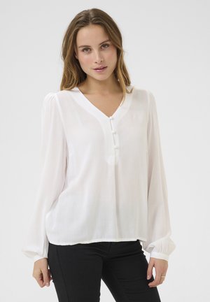 Blouse blanche avec un col en V, des manches longues bouffantes et trois boutons sur le devant. Fabriquée dans un tissu léger et translucide. Texture lisse.