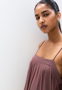 Robe rose sans manches avec des bretelles fines et un design plissé, présentant une coupe décontractée et une texture douce sur un fond neutre.