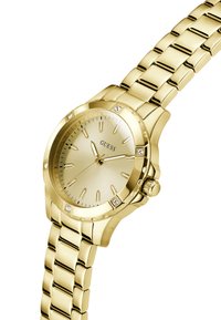 Gold wristwatch with a minimalist dial and diamonds on the bezel, featuring a link bracelet and "GUESS" logo on the face.