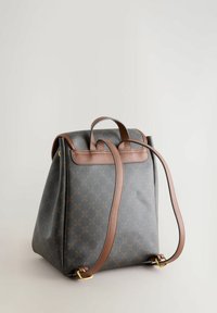 Sac à dos gris à motifs avec des accents et des bretelles en cuir brun, présentant une forme structurée et une poignée supérieure pour des options de transport polyvalentes.