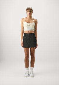 Top corto bianco in maglia con collo all'americana, abbinato a una mini gonna verde scuro con tasche cargo, sneakers bianche e un cappellino beige.