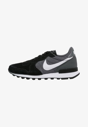 Sneakers Nike con tomaia in suede nero e mesh grigio, swoosh bianco e suola in gomma nera con superficie testurizzata.