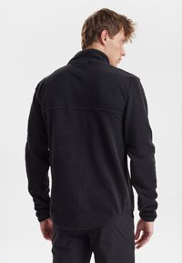 Sort fleece pullover med høj krave, lange ærmer og buet kant. Blød tekstur med en glat overflade og minimale sømme.