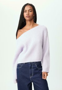 Lila ribbad tröja med off-shoulder-design och långa ärmar, tillsammans med mörkblå jeans med synliga sömmar och fickor.