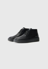 Botas de cuero negro con una textura suave, puntera redonda, diseño con cordones y una suela de goma de bajo perfil con un mínimo de marcas.