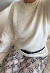 Bela pletena jopica z rebrastim izrezom, kombinirana s karirasto krilo v svetlo roza in črnih odtenkih, poudarjena s črnim pasom.