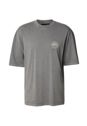 Camiseta gris de algodón con mangas cortas, cuello redondo, que presenta un pequeño logo circular en el lado izquierdo del pecho. Textura suave y ajuste relajado.