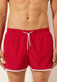 Rote Badehosenshorts mit elastischem Bund und weißer Kordel. Mit weißem Saumverzierungen. Aus leichtem Stoff gefertigt.