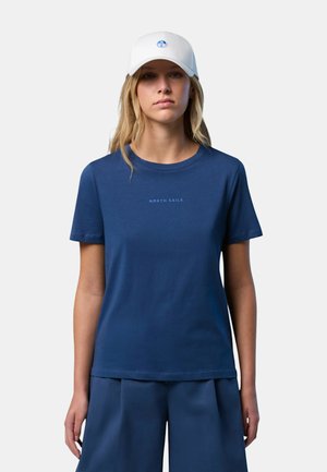 T-shirt in cotone blu navy con scollatura rotonda, maniche corte e testo sottile "NORTH SAILS". Abbinata a pantaloncini blu e un cappellino bianco.