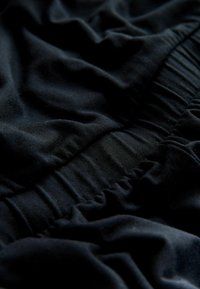 Schwarzer elastischer Bund aus Stoffdetail mit gerafften, gedehnten Abschnitten und sanften Falten, die Textur und Schatten erzeugen.