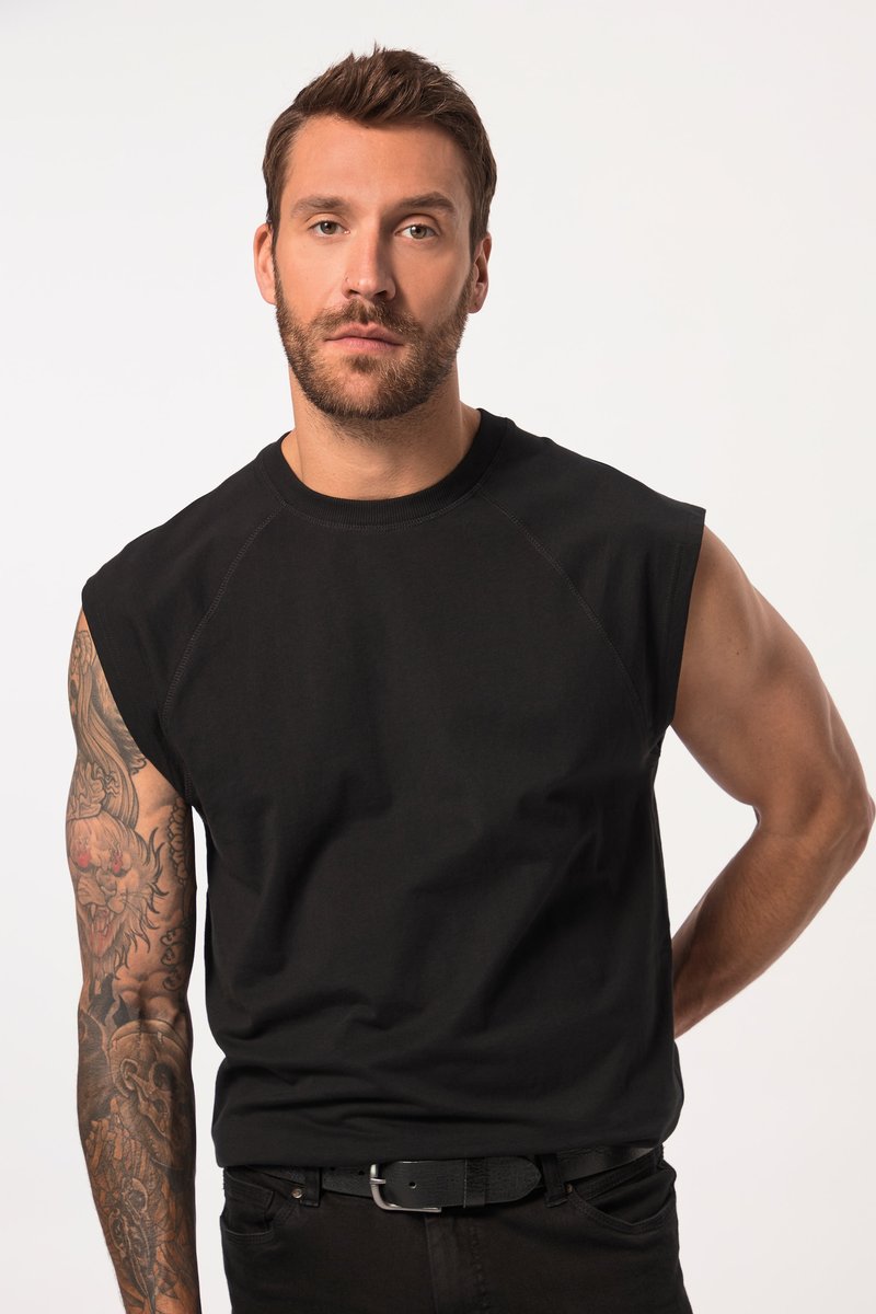Hombre con cabello corto y castaño y barba, vistiendo una camiseta sin mangas negra, mostrando un tatuaje detallado en la manga del brazo izquierdo sobre un fondo liso.