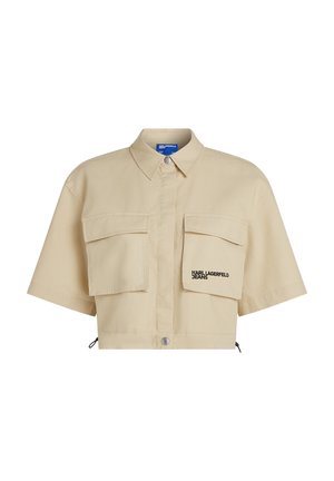Camicetta beige a taglio crop in cotone misto, caratterizzata da due tasche anteriori, chiusura a bottoni e ricamo del logo nero sulla tasca sinistra.