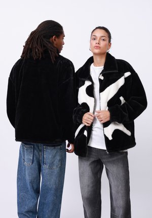 Black plush jacket on the left; white and black patterned fleece jacket on the right with a zip closure and high collar.