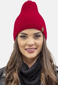 Rød ribbet strikbeanie med spids top, prydet med et struktureret design og et lille sandfarvet lædermærke på siden.