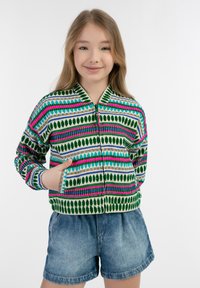 Zippes kardigán zöld, rózsaszín és kék színben, levél- és csíkos mintával; hosszú ujjú, bordázott mandzsettákkal és oldalsó zsebekkel. Alatta farmer rövidnadrág.