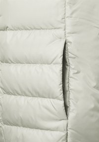 Světlá péřová bunda s horizontálně prošívanými sekcemi, vybavená boční kapsou a hladkým, lesklým povrchem.