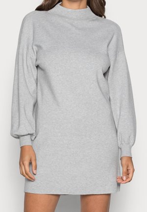 Woman wearing a light grey long-sleeve knit dress with a mock neck and balloon sleeves with fitted cuffs.