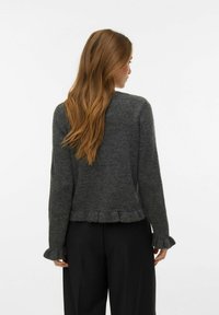 Šedý pletený svetr s volánovým lemem a manžetami. Jednoduchý kulatý výstřih. Má dlouhé rukávy a strukturovaný vzhled.