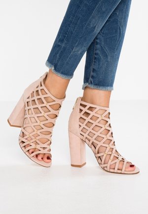 Roze suède pumps met open teen, een kruisbandontwerp en gouden accenten. Voorzien van een stevige hak en uitgesneden zijkanten.