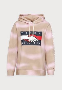 Mikina s kapucí v béžovo-růžovém tie-dye. Obsahuje centrální grafiku propletených rukou a značku; šňůrky na krku.