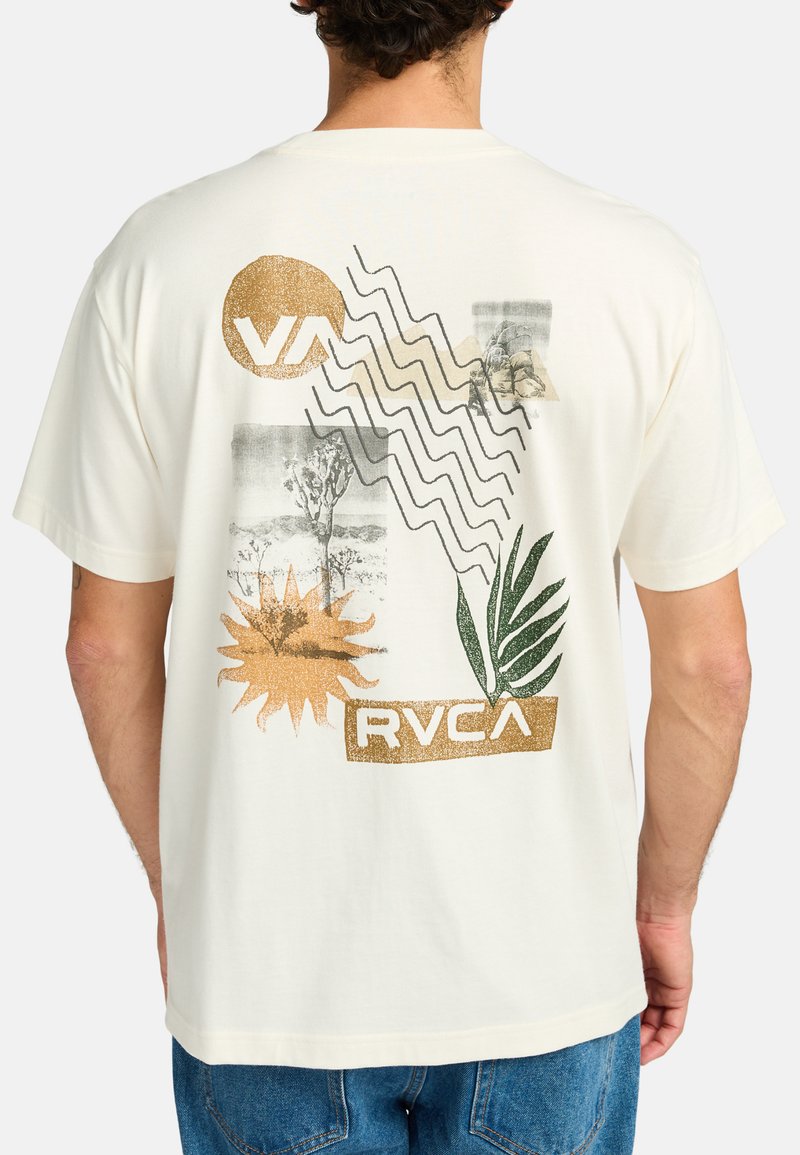 Cream-colored T-shirt featuring multicolored graphic print with abstract designs, a palm leaf, and brand logos in gold and green accents.