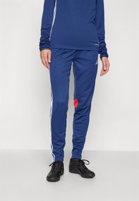 Blue athletic pants with white side stripes, featuring red accents. Made of soft material, designed for comfort and mobility.
