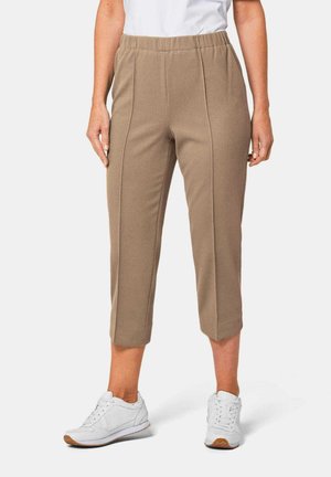 Pantalons beige cropped avec une texture côtelée et des détails sur les coutures latérales, associés à des chaussures de sport blanches. Taille élastique pour plus de confort.