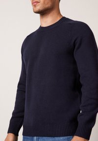 Mörkblå munktröja med rund hals gjord av stickad tyg, med ribbade ärmslut och nederkant, slät textur och en figurnära silhuett.