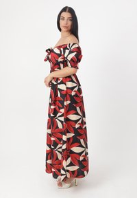 Maxikjole i sort stof med blomster mønster i rød og creme. Off-shoulder design med puffede ærmer og smocket liv.