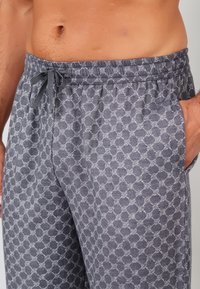 Rekbare grijze loungebroeken met een geometrisch patroon, elastische tailleband en trekkoord. Voorzien van zijzakken voor extra gemak.