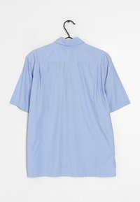 Kortärmad ljusblå skjorta i mjuk tyg. Har en krage, bakfickor och en rak fåll. Hänger på en svart krok.