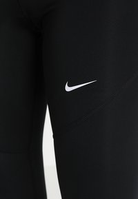 Svarta leggings i stretchtyg med en vit Nike-swoosh-logga på låret. Slät yta med en åtsittande design och platta sömmar.
