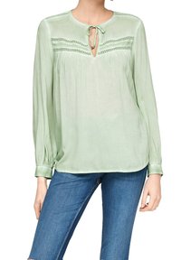 Blusa verde chiaro con maniche lunghe, scollatura rotonda, dettaglio con fiocco alla scollatura, fronte plissettato e accenti in pizzo sul petto. Tessuto morbido.