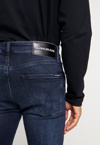 Jeans de mezclilla oscura con una textura suave. Incluyen un parche de cuero con la marca en la parte posterior de la cintura y un pequeño bolsillo delantero.